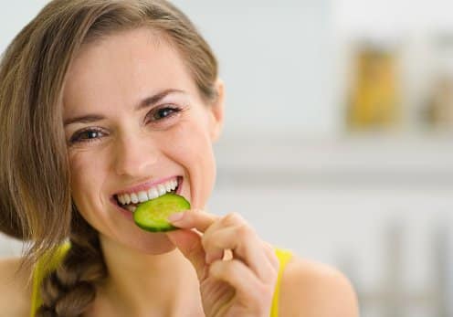 Happy young woman eating slice of cucumber