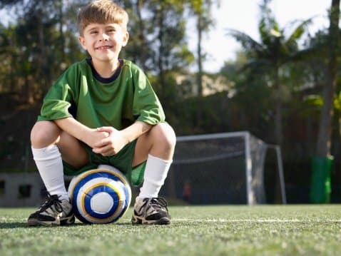 Boy sitting on soccer ball (portrait, low angle view)