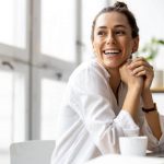 Smiling professional woman working on a laptop in a bright office setting.