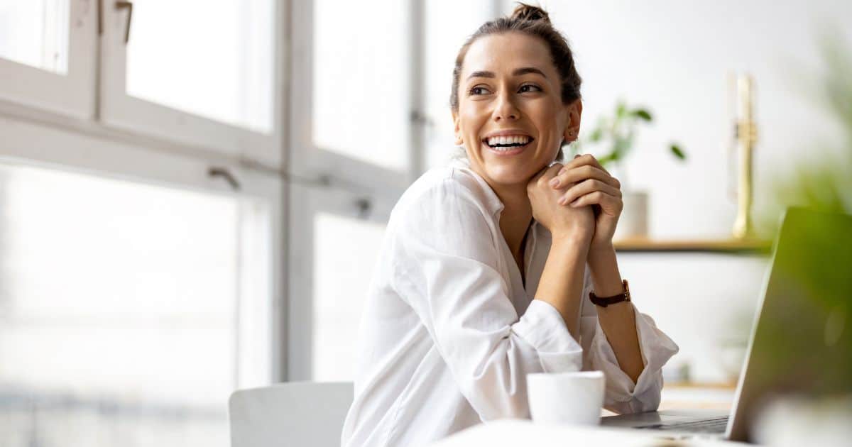 Smiling professional woman working on a laptop in a bright office setting.